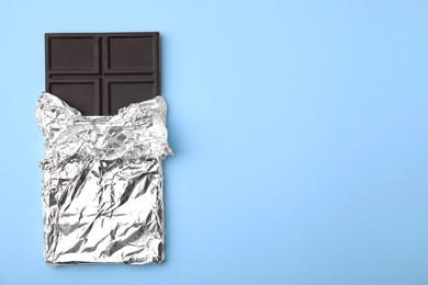 Photo of Tasty chocolate bar on light blue background, top view. Space for text