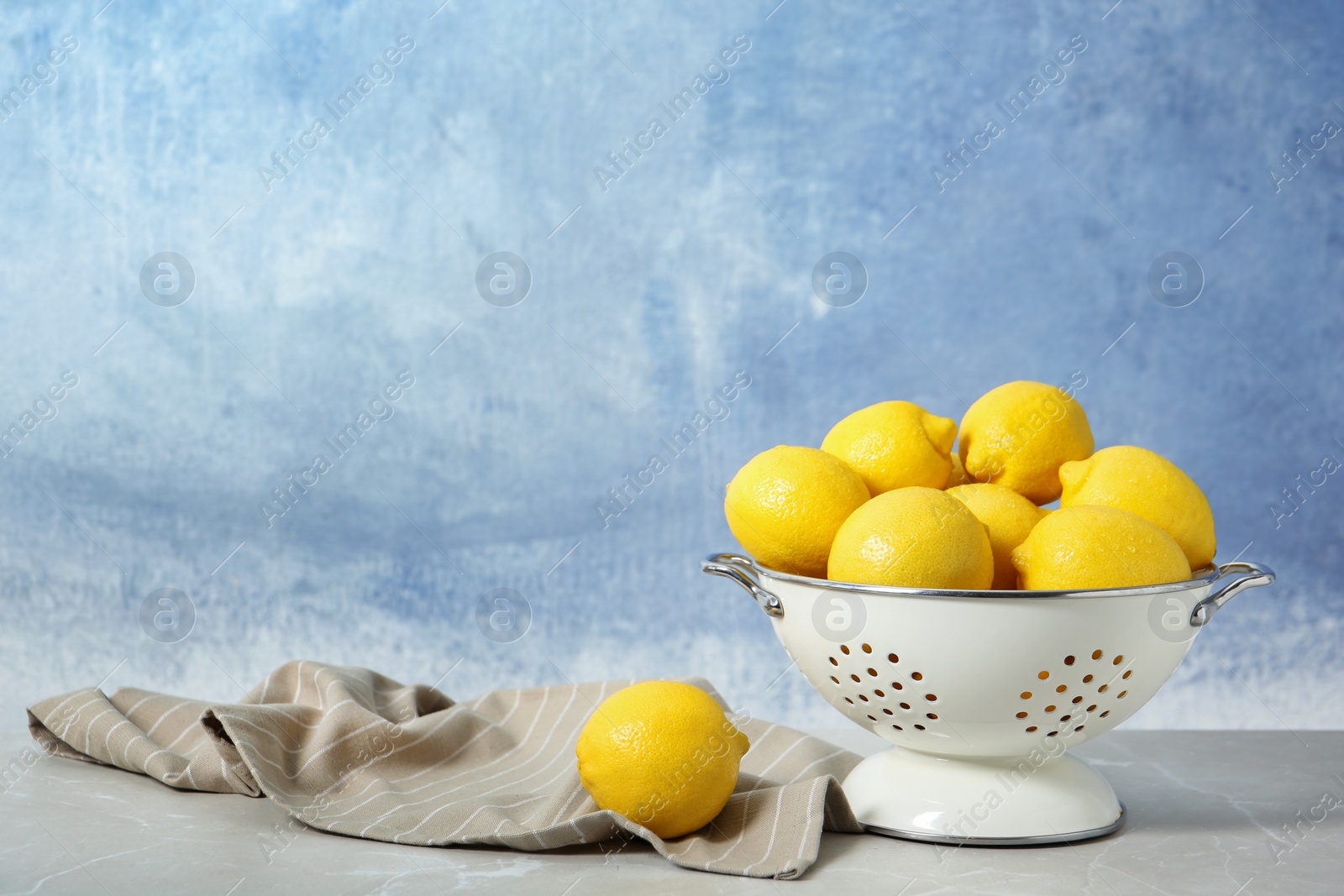 Photo of Colander with ripe lemons on table against color background