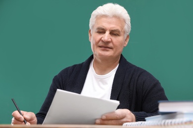 Portrait of senior teacher at table against green chalkboard