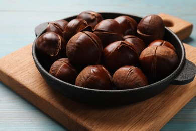 Fresh edible sweet chestnuts in frying pan on light blue wooden table, closeup