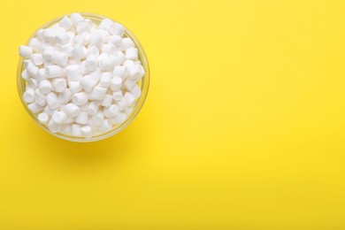 Photo of Glass bowl with delicious marshmallows on yellow background, top view. Space for text