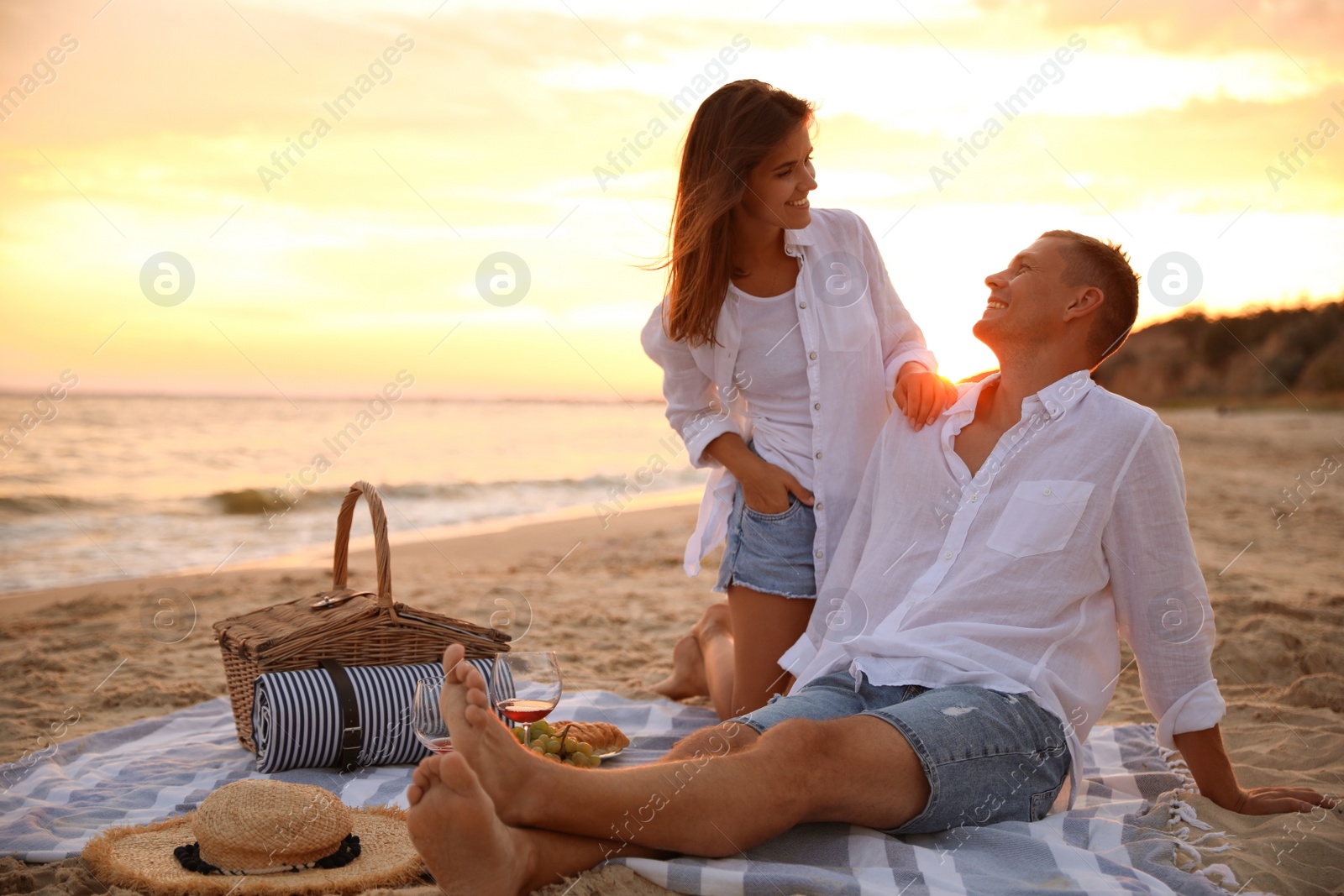 Photo of Lovely couple having romantic picnic on beach at sunset