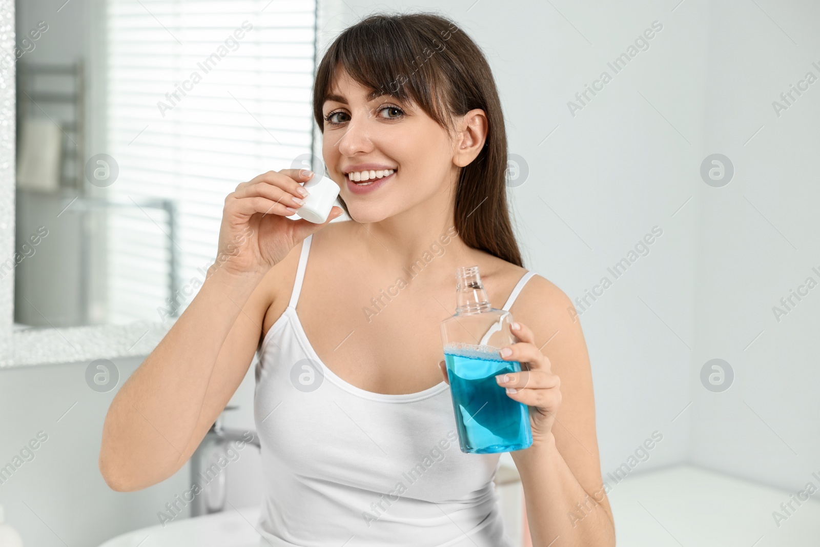 Photo of Young woman using mouthwash in bathroom. Oral hygiene