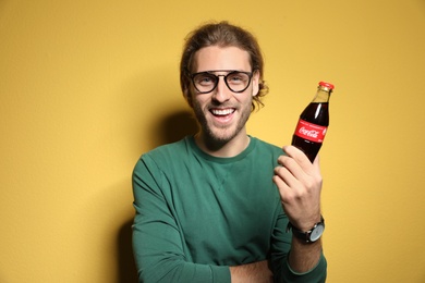 Photo of MYKOLAIV, UKRAINE - NOVEMBER 28, 2018: Young man with bottle of Coca-Cola on color background
