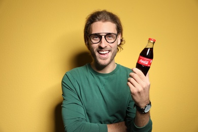 MYKOLAIV, UKRAINE - NOVEMBER 28, 2018: Young man with bottle of Coca-Cola on color background