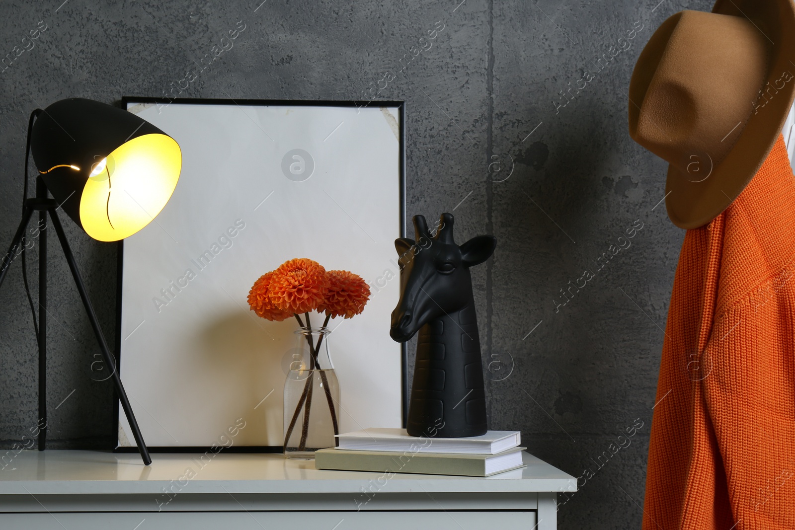 Photo of Stylish decor, vase with flowers, picture and desk lamp on white table near grey wall in hallway. Interior design