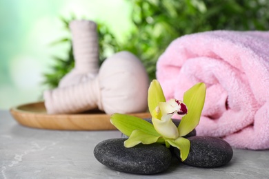 Spa stones, exotic flower, towel and herbal bags on grey marble table, space for text