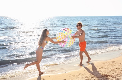 Photo of Happy young couple in beachwear playing with inflatable ball on seashore