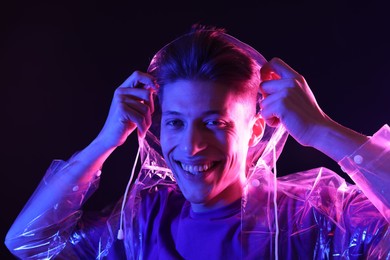 Young man wearing clear coat on dark background in neon lights