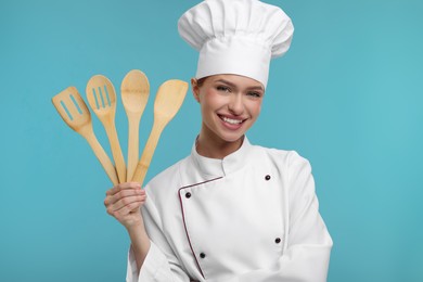Photo of Happy chef in uniform holding wooden utensils on light blue background