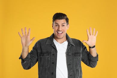 Man showing number ten with his hands on yellow background