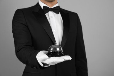 Photo of Butler holding service bell on grey background, closeup