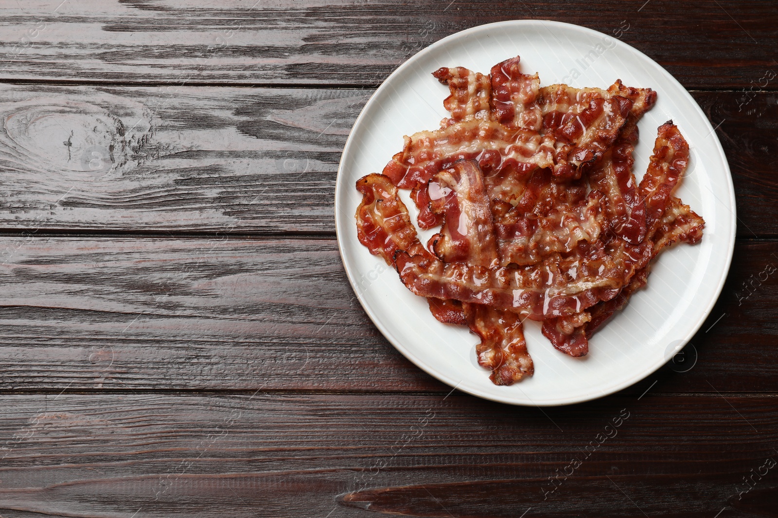 Photo of Slices of tasty fried bacon on wooden table, top view. Space for text