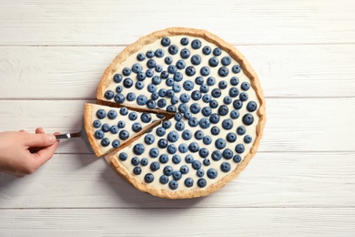 Woman taking piece of tasty blueberry cake on wooden table, top view