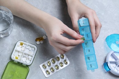 Woman putting pill into plastic box at grey marble table, top view