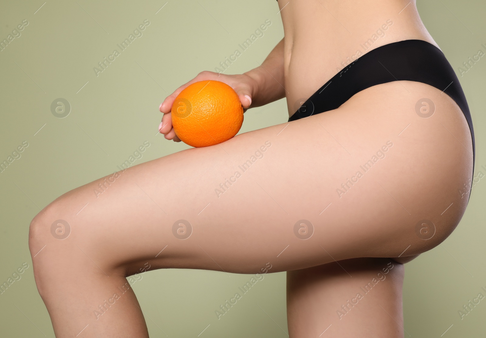 Photo of Closeup view of slim woman in underwear with orange on light green background. Cellulite problem concept