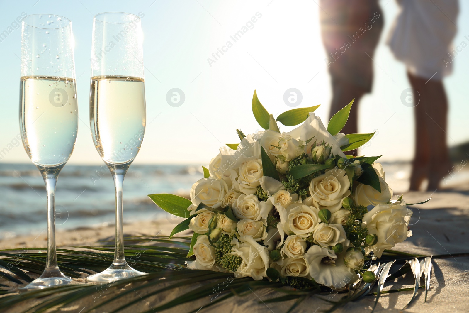 Photo of Beautiful wedding bouquet, glasses of champagne and couple on sandy beach