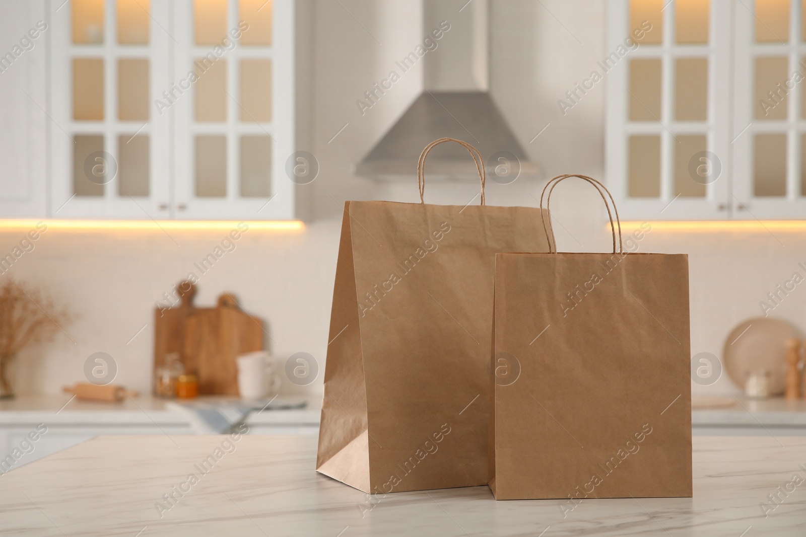 Photo of Paper shopping bags on white marble table in kitchen. Space for text