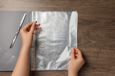 Woman putting punched pocket into file folder at wooden table, top view