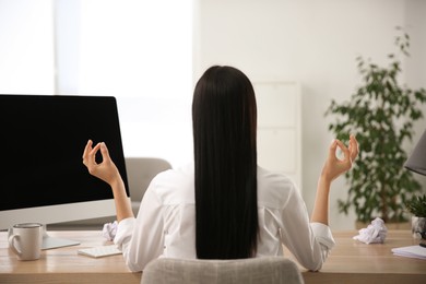 Woman meditating at workplace in office, back view