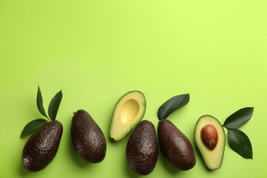 Photo of Ripe avocadoes and leaves on green background, flat lay. Space for text