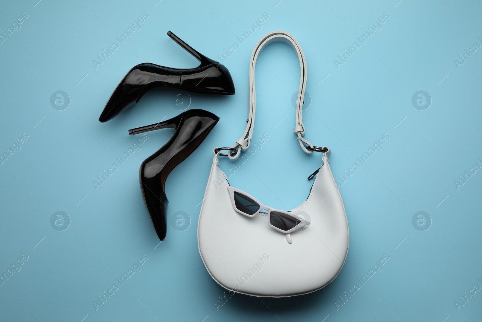 Photo of Stylish woman's bag, shoes and sunglasses on light blue background, flat lay