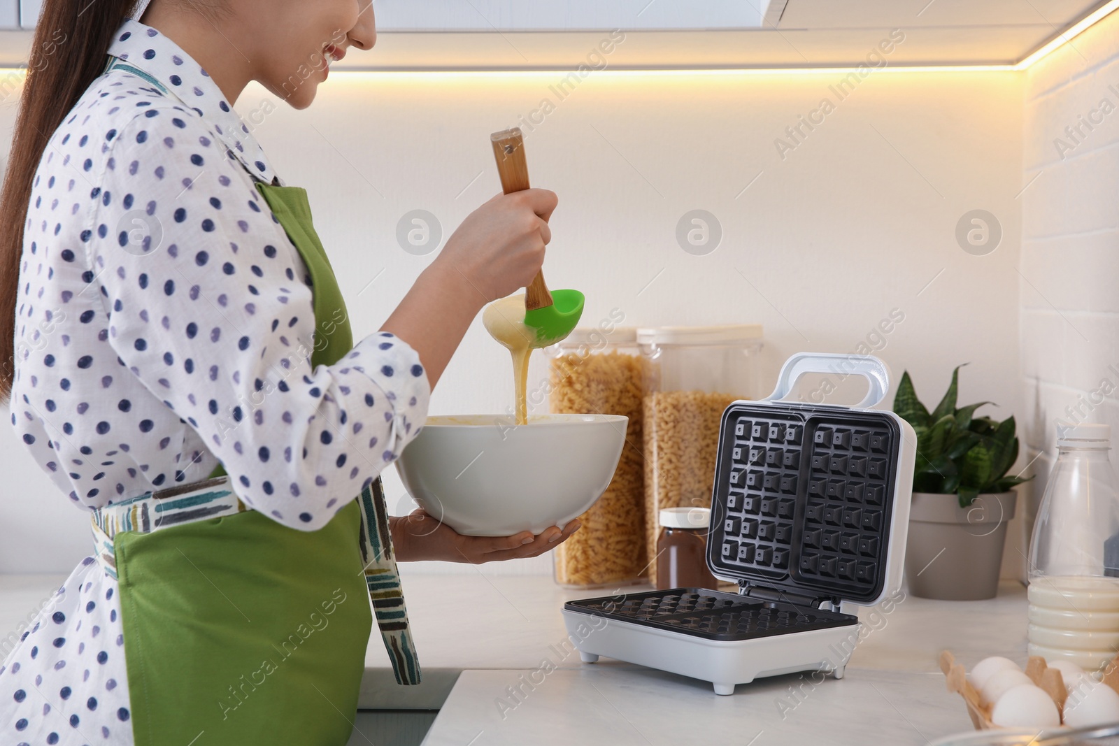 Photo of Woman preparing dough near Belgian waffle maker in kitchen, closeup