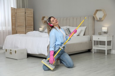 Woman in headphones with mop singing while cleaning at home