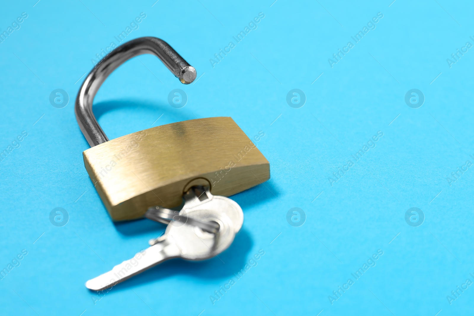 Photo of Steel padlock with keys on light blue background, closeup. Space for text