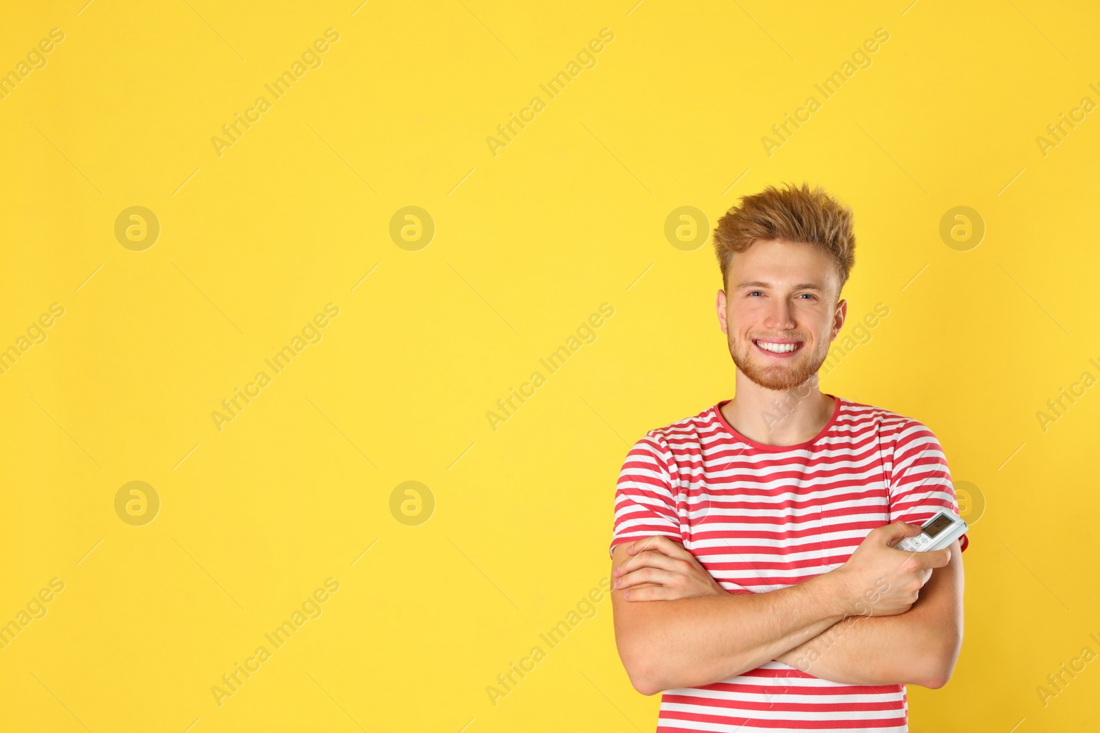 Photo of Young man with air conditioner remote on yellow background. Space for text