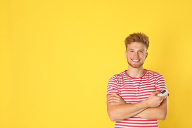 Photo of Young man with air conditioner remote on yellow background. Space for text