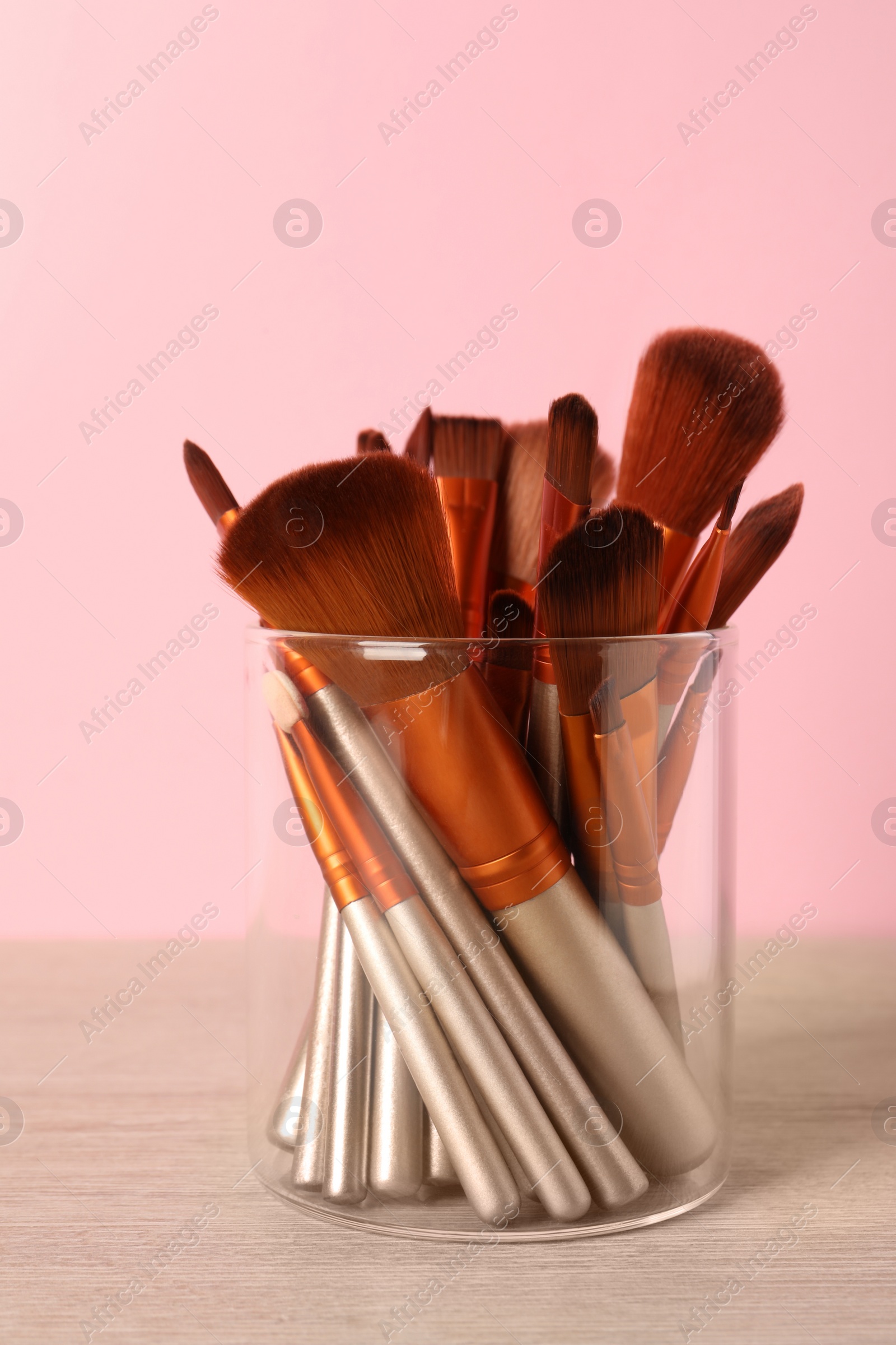 Photo of Set of professional makeup brushes on wooden table against pink background