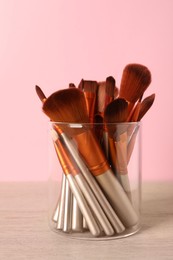 Set of professional makeup brushes on wooden table against pink background