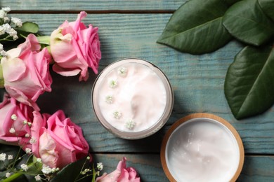 Jar of face cream and pink roses on light blue wooden table, flat lay