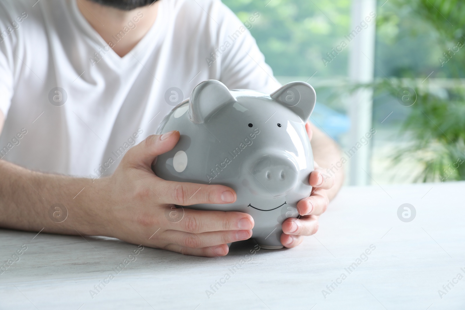 Photo of Man with piggy bank at white table indoors, closeup