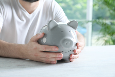 Photo of Man with piggy bank at white table indoors, closeup