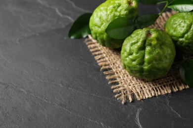 Photo of Fresh ripe bergamot fruits with green leaves on black table, space for text
