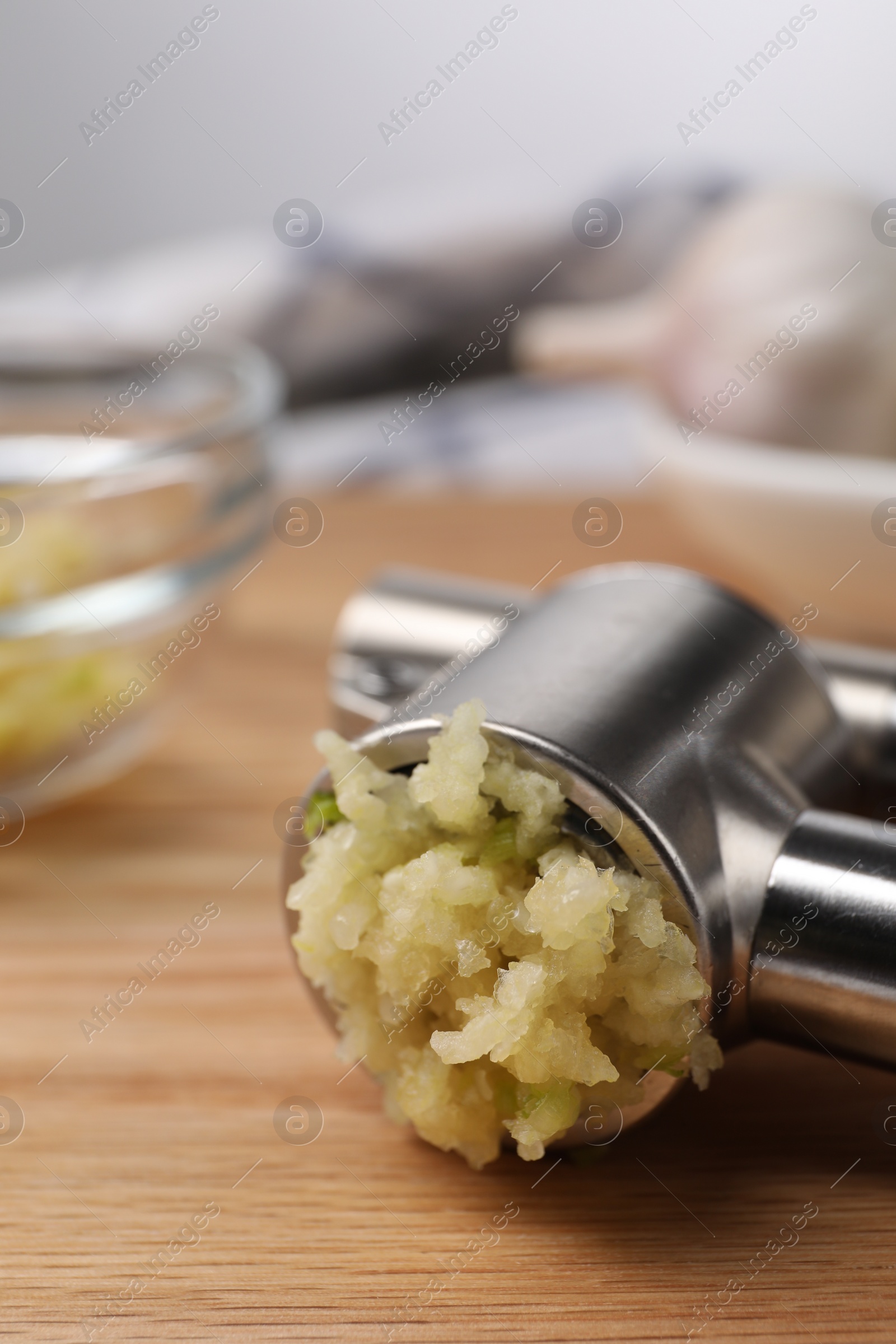 Photo of One metal press with crushed garlic on wooden table, closeup