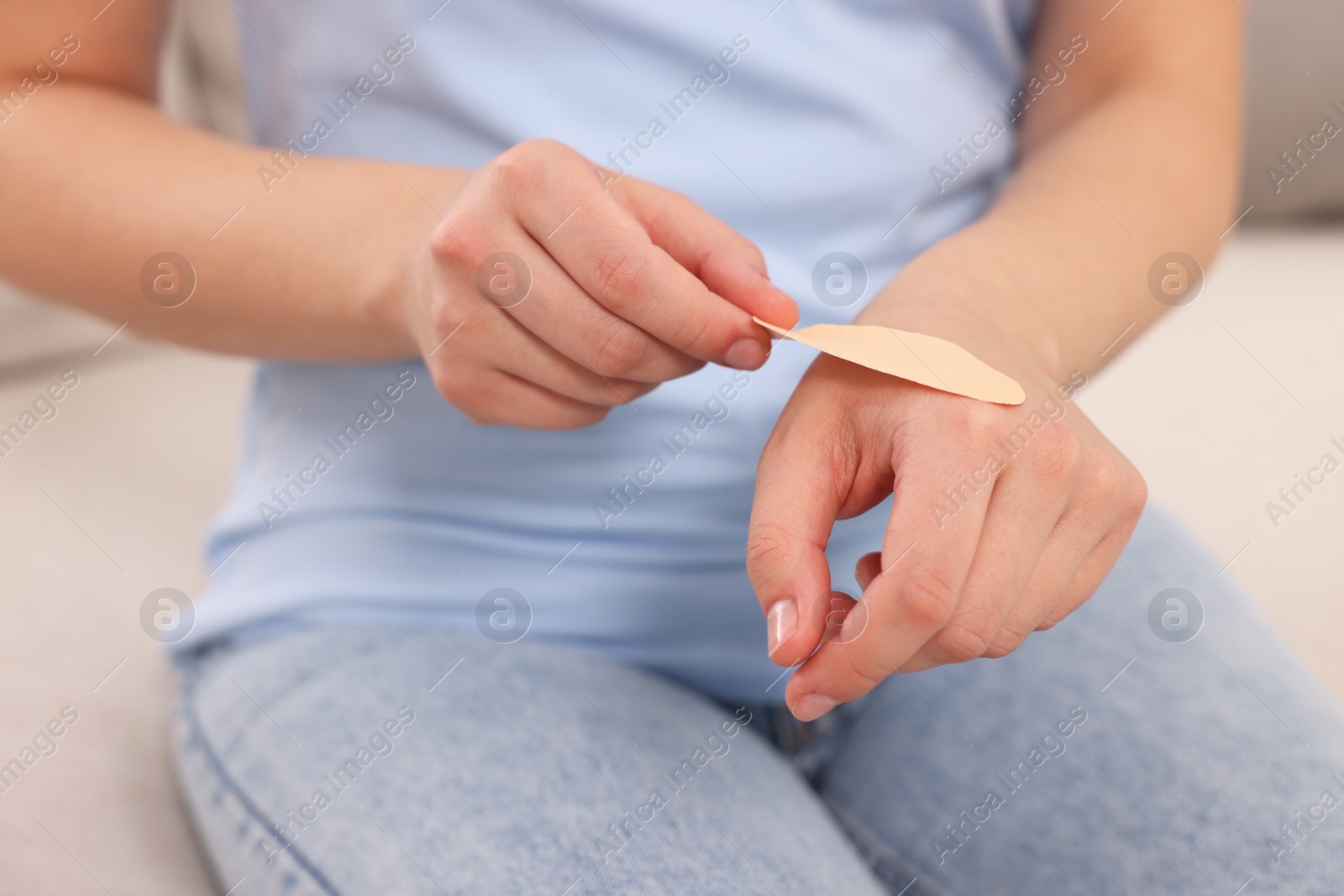 Photo of Woman putting sticking plaster onto hand on sofa, closeup