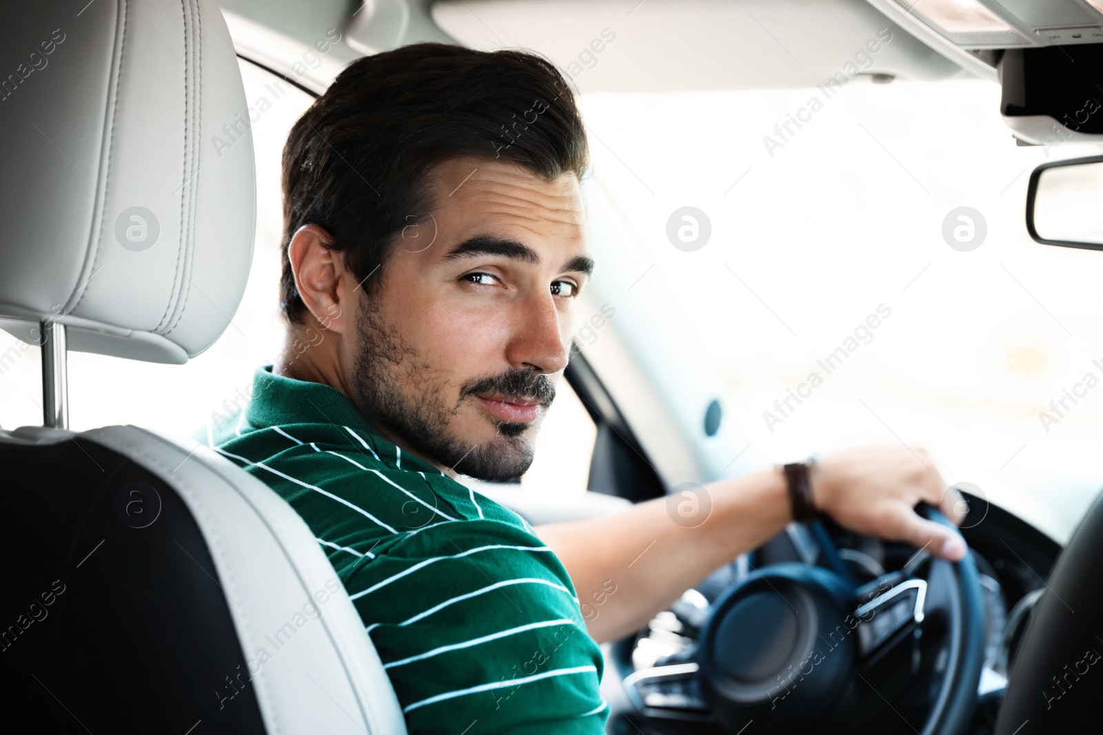 Photo of Attractive young man driving luxury car, view from backseat