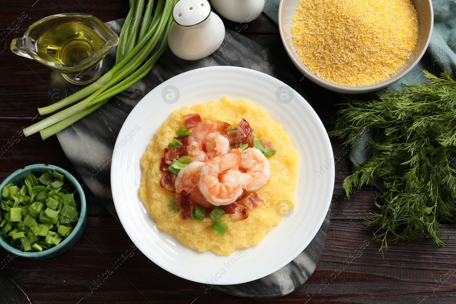 Photo of Plate with fresh tasty shrimps, bacon, grits and green onion on dark wooden table, flat lay