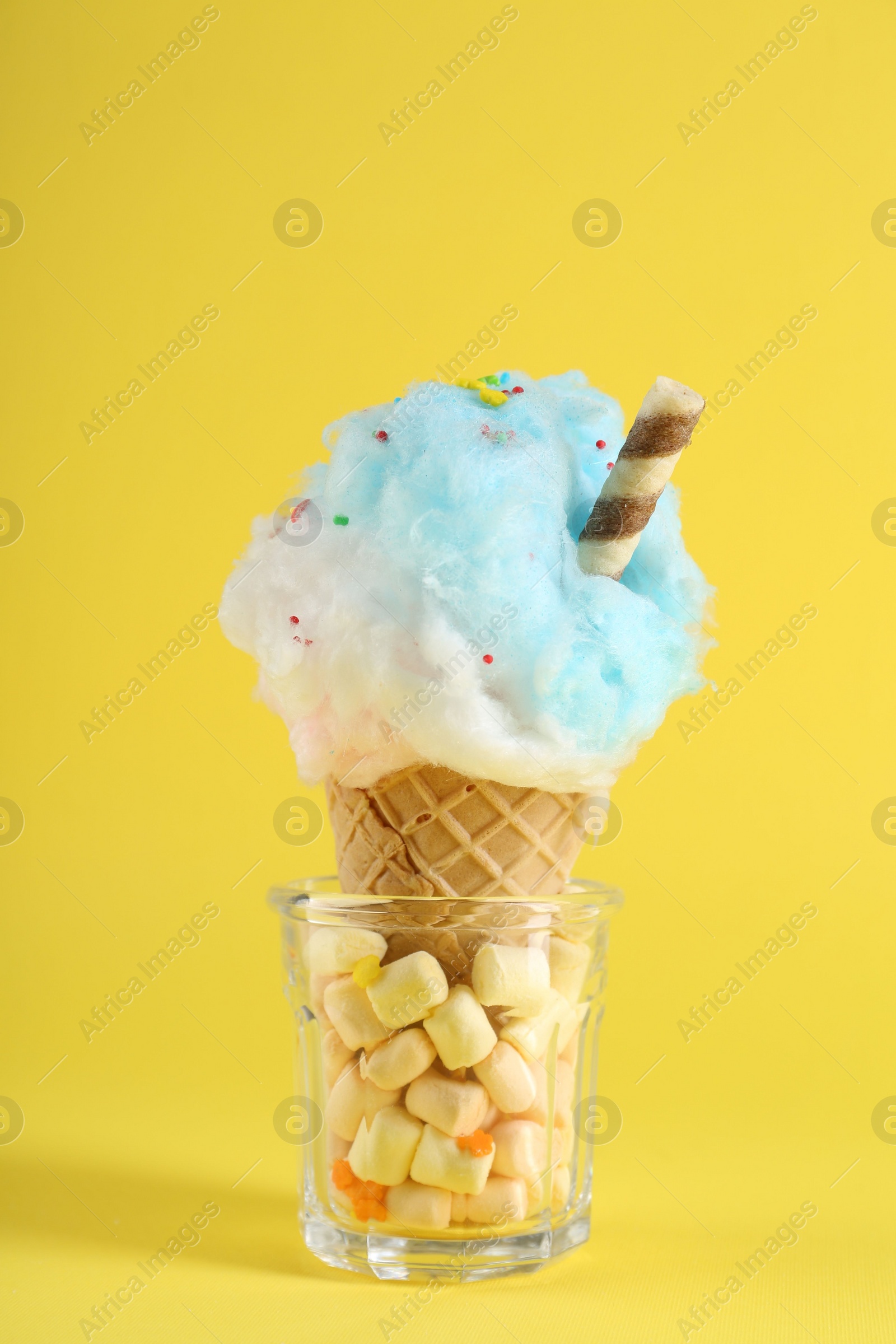 Photo of Sweet cotton candy in waffle cone on yellow background