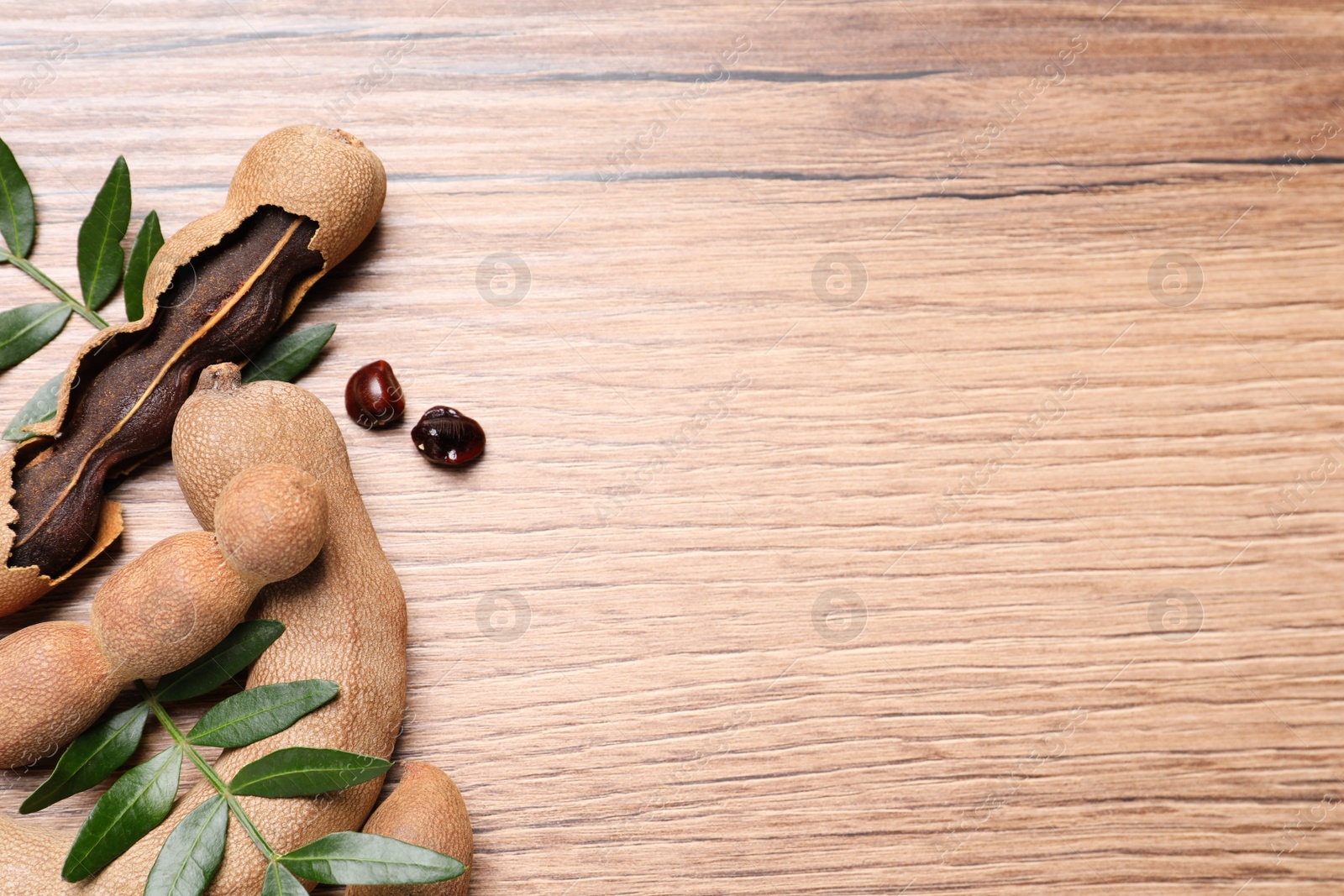 Photo of Delicious ripe tamarinds and leaves on wooden table, flat lay. Space for text