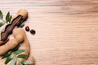 Delicious ripe tamarinds and leaves on wooden table, flat lay. Space for text