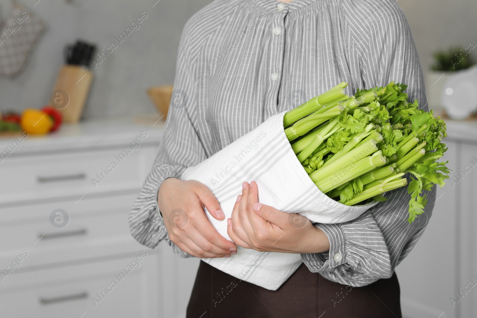 Photo of Woman with fresh green celery in kitchen, closeup. Space for text
