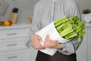 Photo of Woman with fresh green celery in kitchen, closeup. Space for text