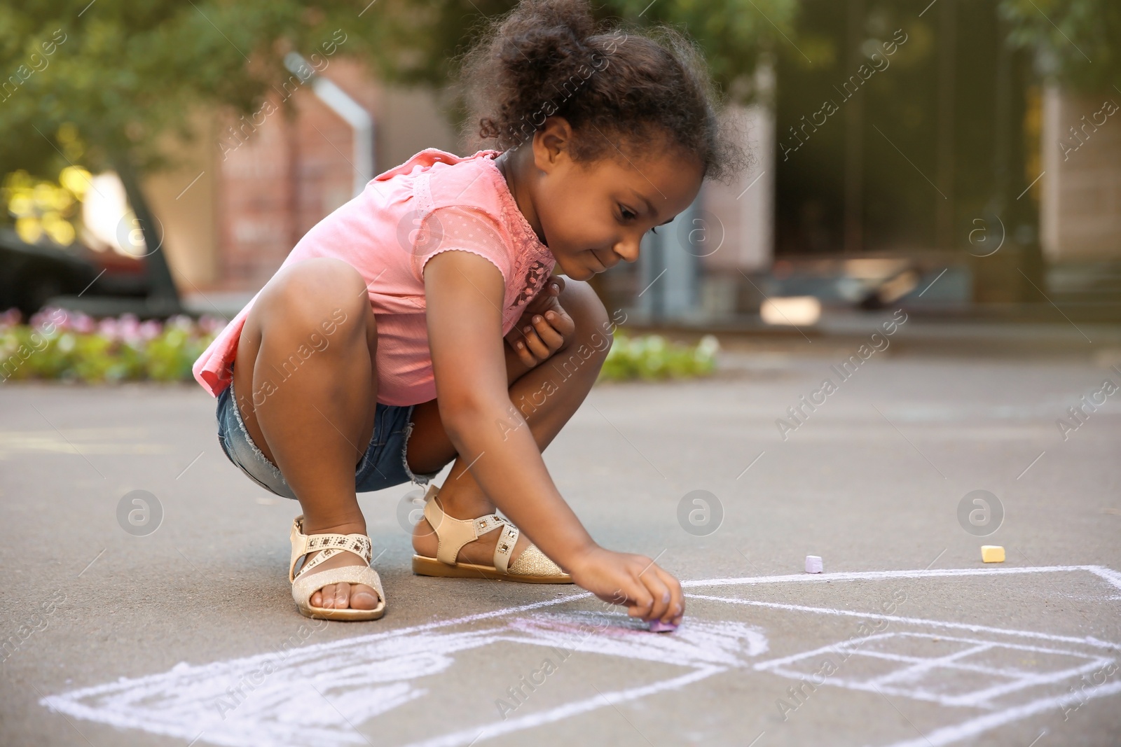 Photo of Little African-American child drawing house with chalk on asphalt