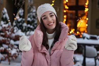 Portrait of smiling woman with burning sparkles on snowy city street