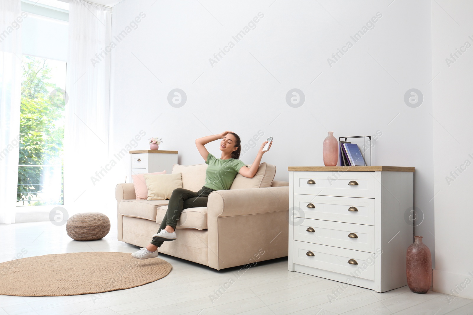 Photo of Happy young woman switching on air conditioner with remote control at home