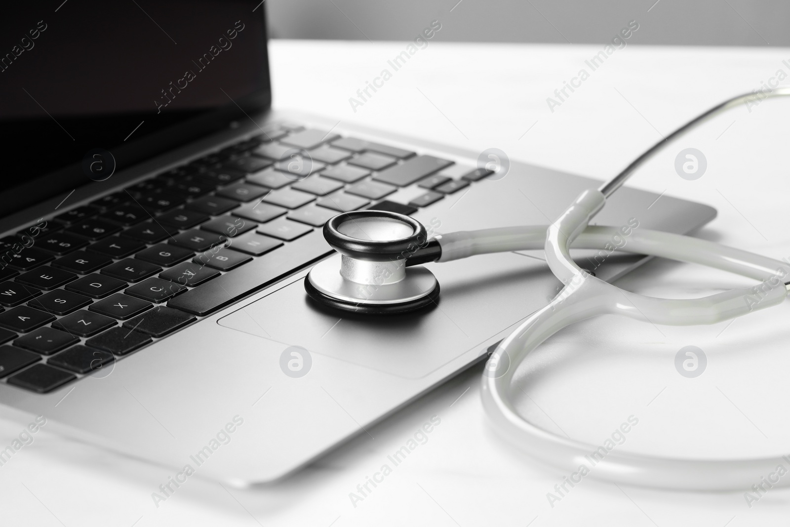 Photo of Modern laptop and stethoscope on white table, closeup